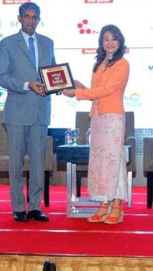 Teresa Hii in a peach jacket presenting a framed token to a guest on a conference stage